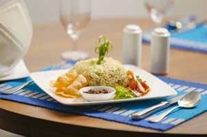 Un plato de comida con arroz, verduras y un pequeño recipiente de salsa sobre una base azul.