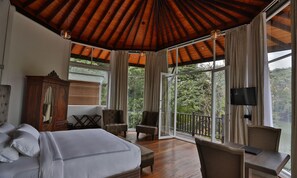Un dormitorio con una cama grande, techo de madera, televisor y balcón con vistas a árboles.