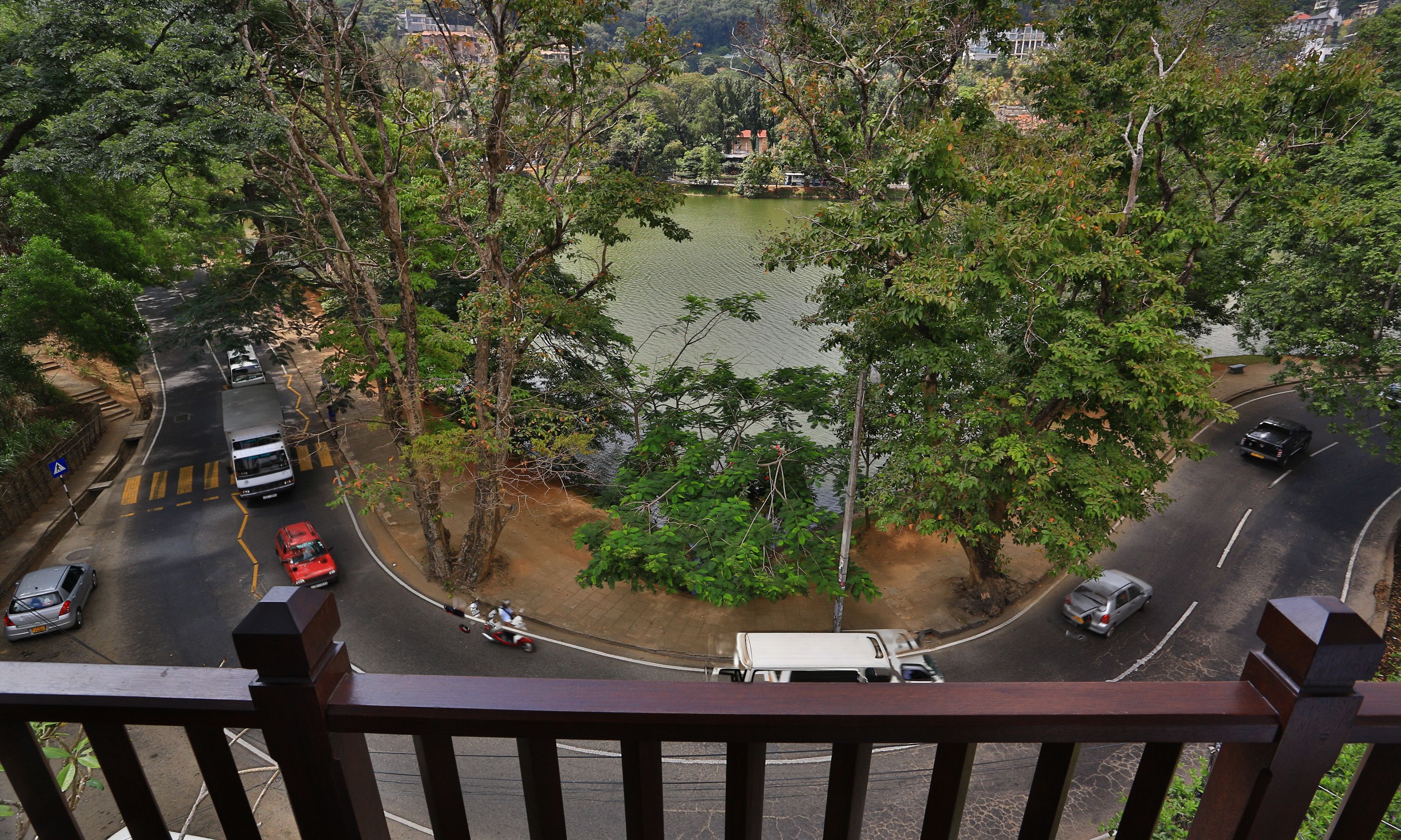 A view of a road curving around a lake with trees and buildings in the background.