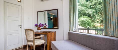 A room with a wooden desk, a chair, a bed, a mirror, and a window with a view of trees.