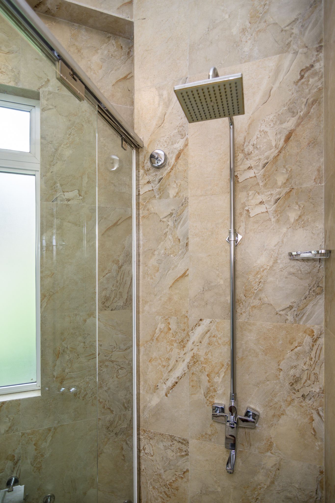 A modern bathroom with a glass-enclosed shower, a marble wall, and a chrome showerhead.