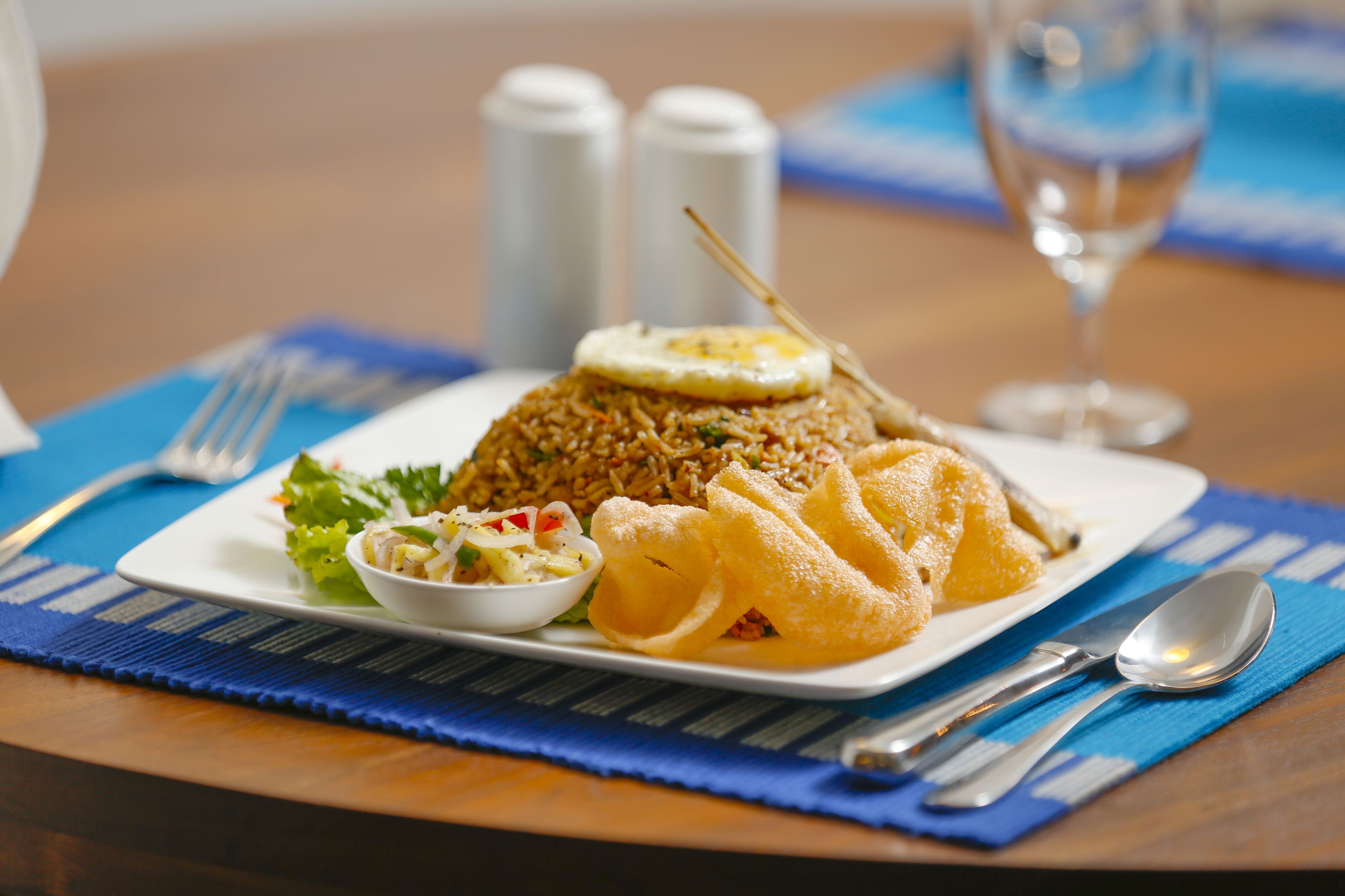 Prato de arroz frito com um ovo frito por cima, acompanhado de uma salada pequena e dois wontons fritos.