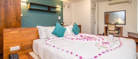 Habitación de hotel con cabecera de madera, un escritorio con una silla, un espejo y una cama con cubrecama blanco y almohadas turquesa.