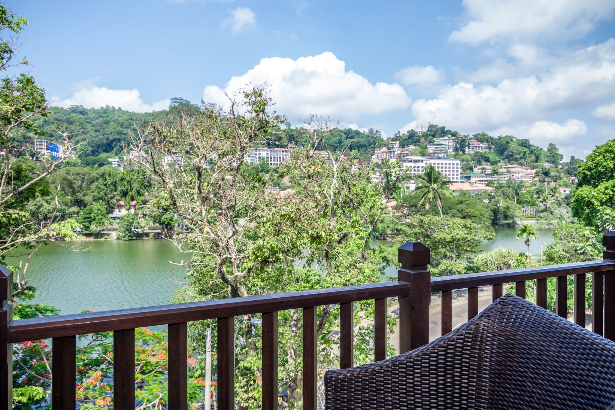 A view from a balcony overlooking a lake with surrounding greenery and buildings in the background.