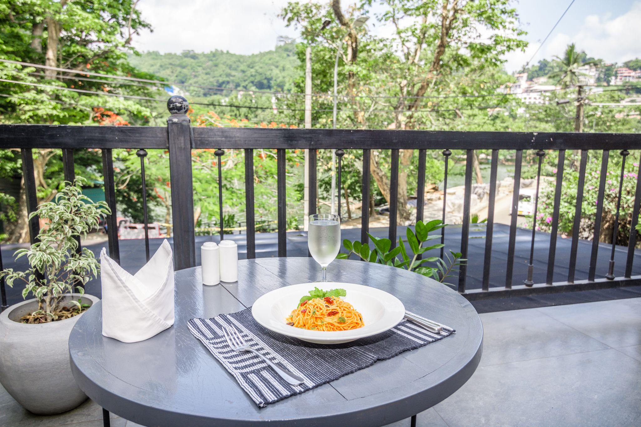 A round table with a plate of spaghetti, a glass of white wine, salt and pepper shakers, and a folded napkin on a black mat.