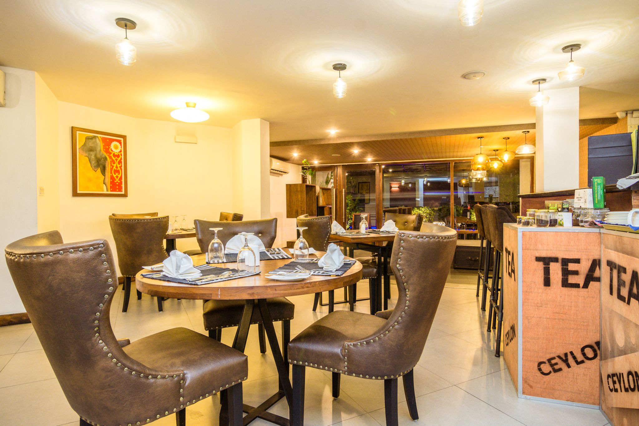 Un restaurante con mesas redondas, sillas de cuero marrón y una barra con la leyenda 'TEA'.