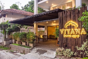 Entrada de un hotel boutique con un letrero de madera, asientos al aire libre y plantas en macetas.