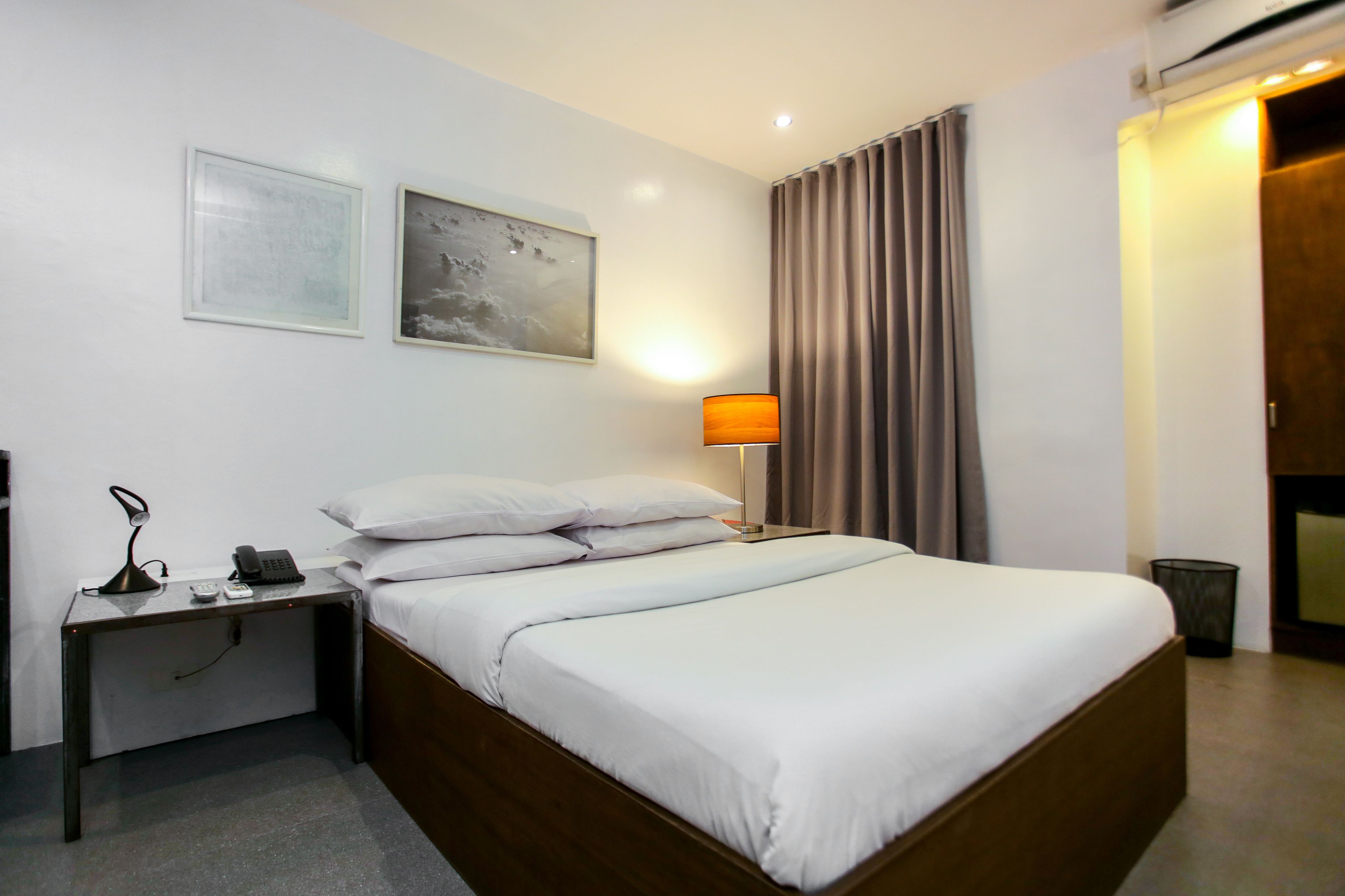 Habitación de hotel con una cama individual, una mesita de noche con lámpara, un teléfono y un marco de fotos.