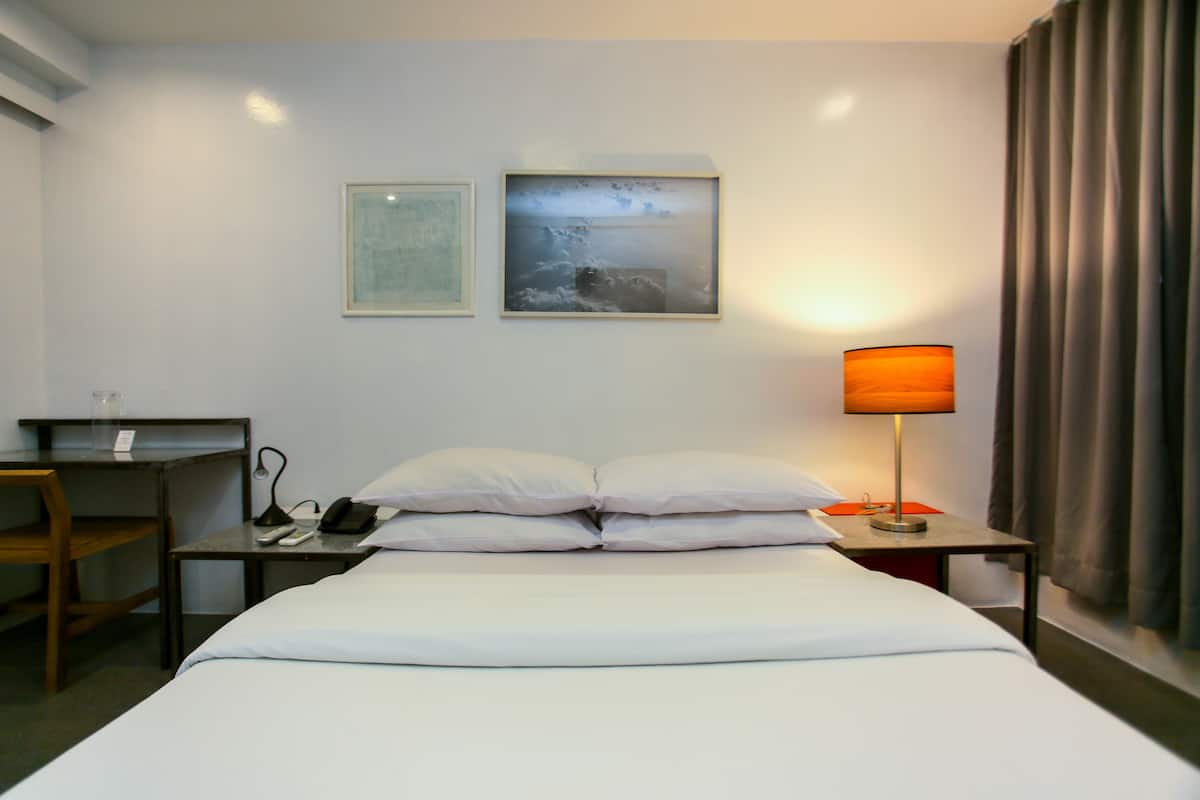 Une chambre d’hôtel avec un lit, un bureau, une chaise, une lampe et deux tableaux encadrés au mur.
