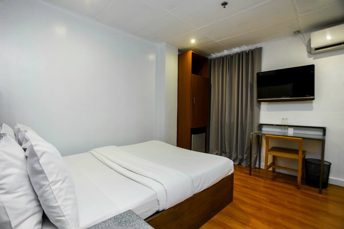Une chambre d’hôtel avec un lit, un bureau, une télévision et une fenêtre avec des rideaux.