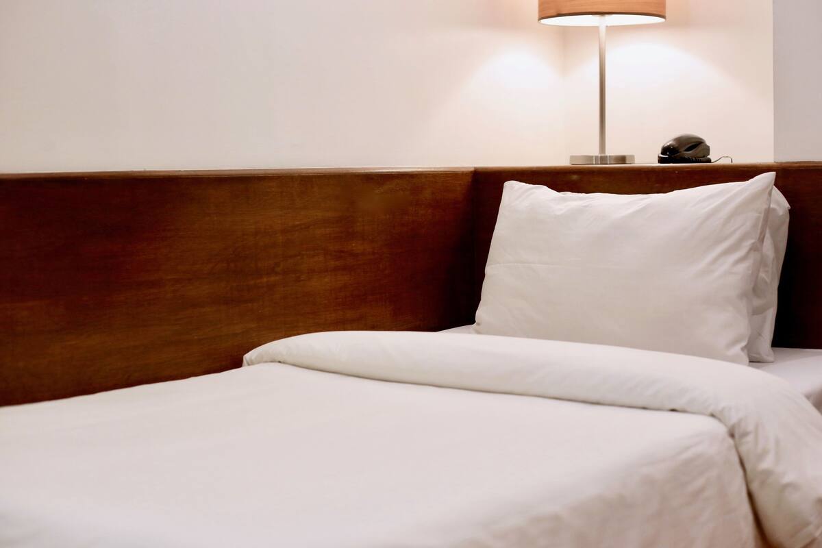 Une chambre d’hôtel avec une tête de lit en bois, un lit blanc et une lampe de chevet.