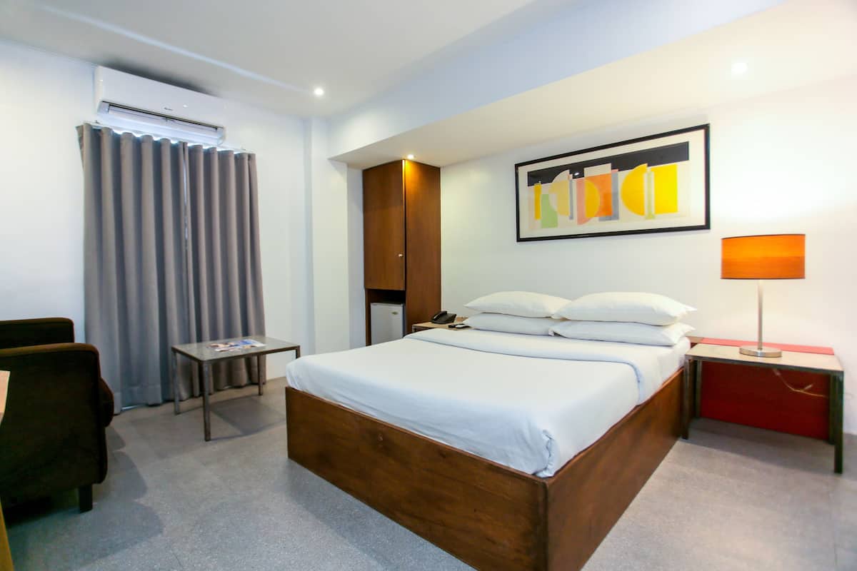 Une chambre d’hôtel avec un lit en bois, un bureau, une chaise, un appareil de climatisation, une armoire et un tableau au mur.