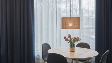 A dining area with a round table, four chairs, a vase with flowers, and a hanging lamp.