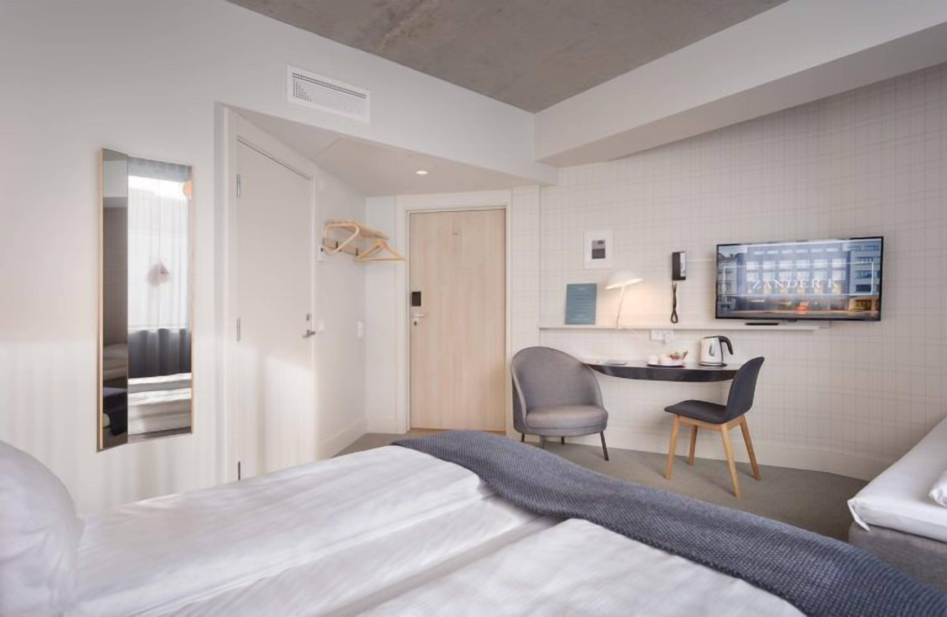 A hotel room with a bed, a desk with a chair, a television, and a wardrobe.