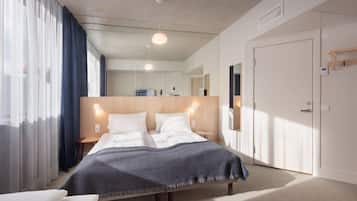 A modern hotel room with a large bed, a bedside table, a nightstand, a wardrobe, and a mirror.