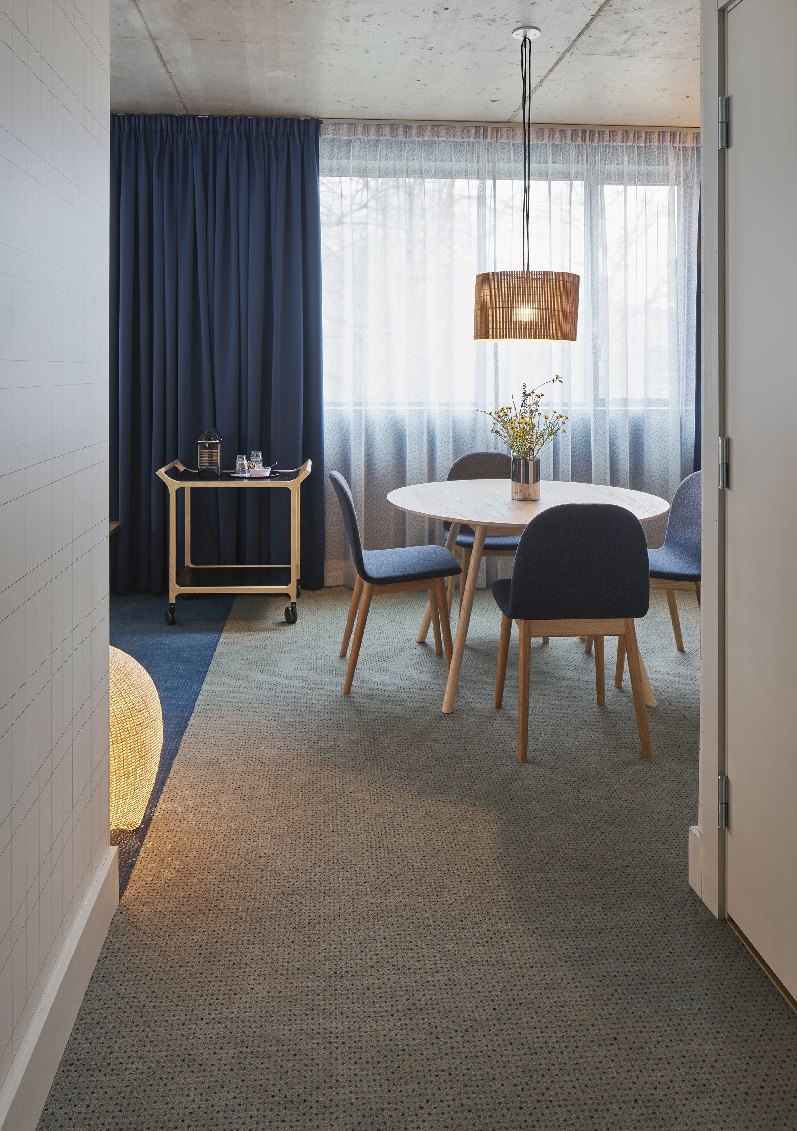Un espace repas comprenant une table ronde, des chaises, un luminaire suspendu et un chariot contenant divers objets.