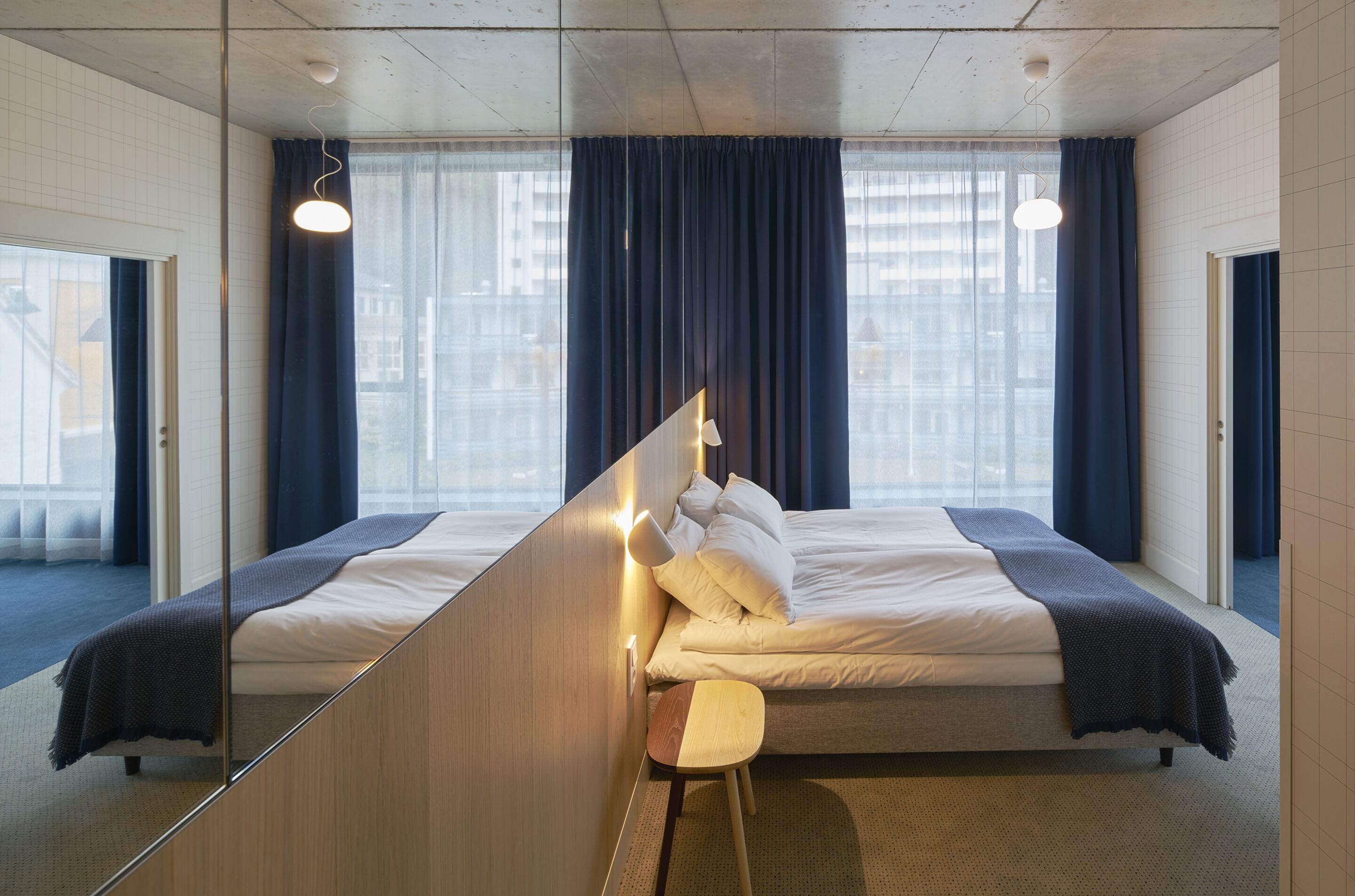 Una habitación de hotel moderna con una cama grande, un taburete pequeño y un espejo.