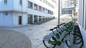 A row of green and white OBOS bicycles parked along a sidewalk next to a white building with large windows.