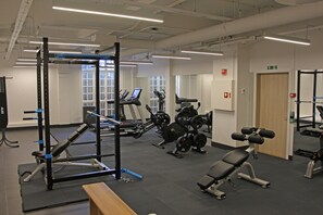 Ein Fitnessraum mit unterschiedlichen Trainingsgeräten, darunter Laufbänder, Kraftgeräte und eine Bank.
