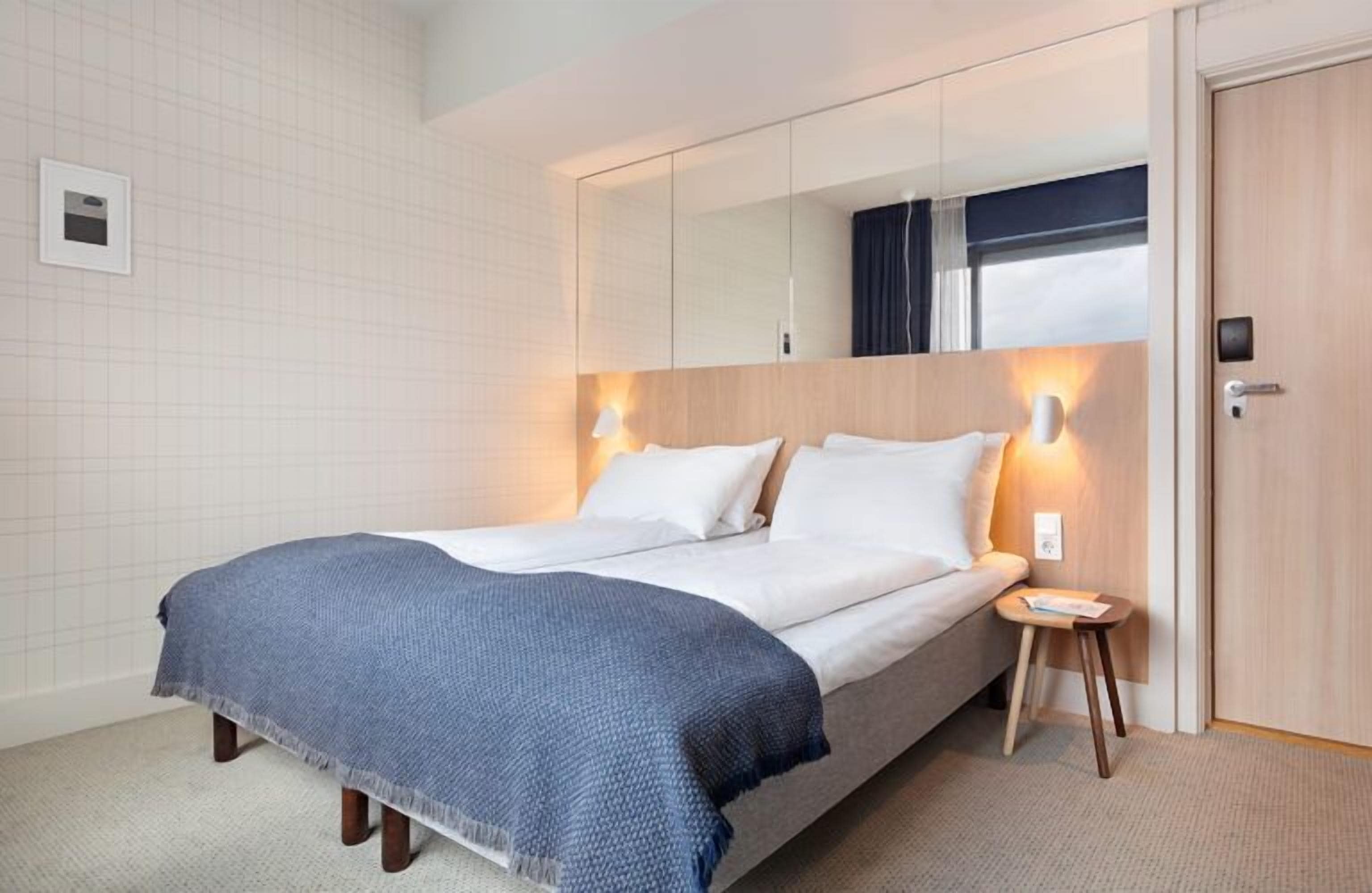Ein modernes Hotelzimmer mit einem großen Bett, einem Nachttisch, einem Spiegel und einem Kleiderschrank.