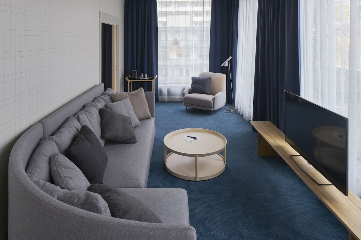 A modern living room with a curved grey sofa, a round coffee table, and a small side table with a lamp.