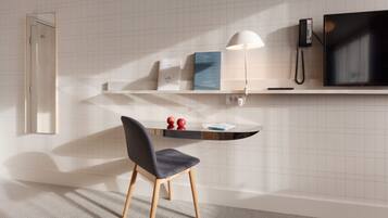 A modern hotel room with a desk, chair, lamp, and a mounted television.