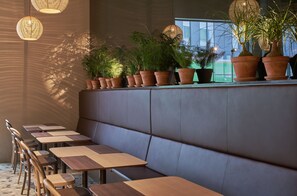 Ein modernes Café mit einer langen Sitzbank, Holztischen und Kübelpflanzen.