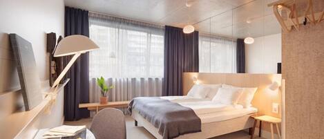 Una habitación de hotel moderna con cama, mesitas de noche, un escritorio con lámpara, una silla y una bandeja de frutas.