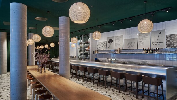 A modern bar area with a long wooden counter, multiple stools, and hanging spherical light fixtures. - Zander K Hotel (Bergen)