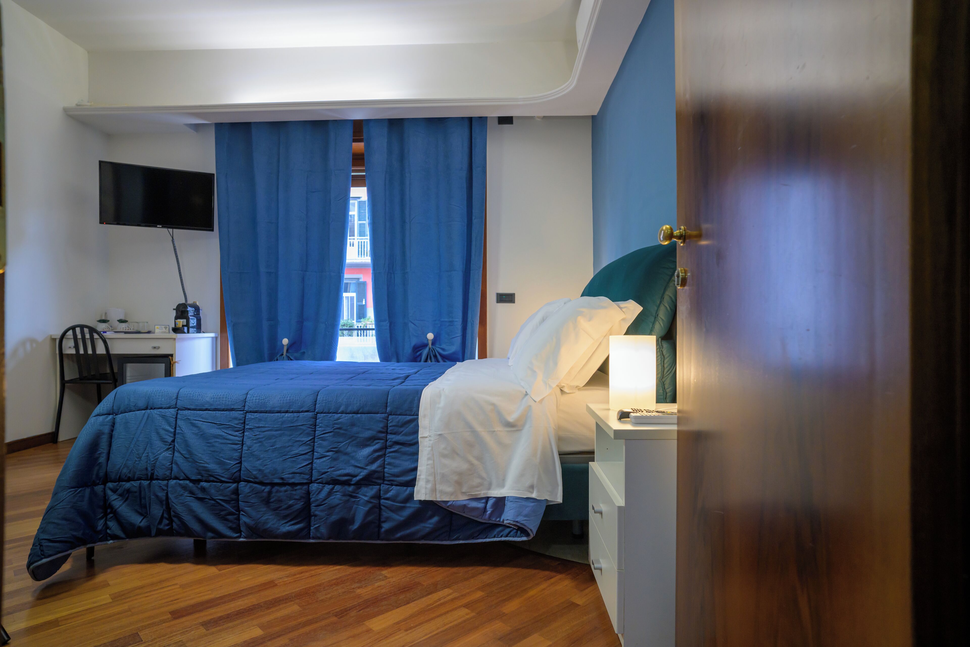 Un dormitorio con cama, escritorio, silla, televisor y ventana con cortinas.