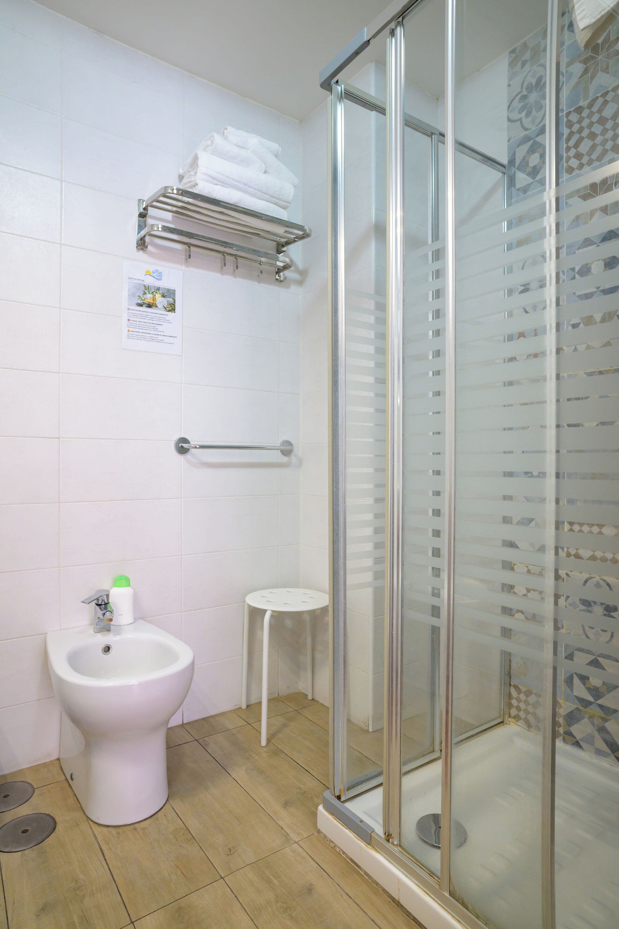 A bathroom with a glass-enclosed shower, a white pedestal sink, and a towel rack.