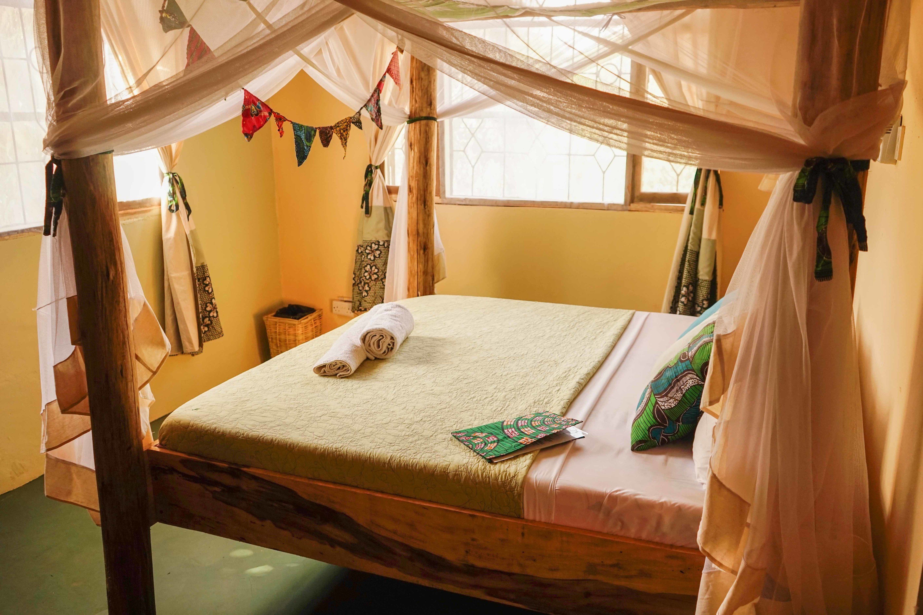 A room with a bed under a canopy, a window, and a wall with hanging textiles.