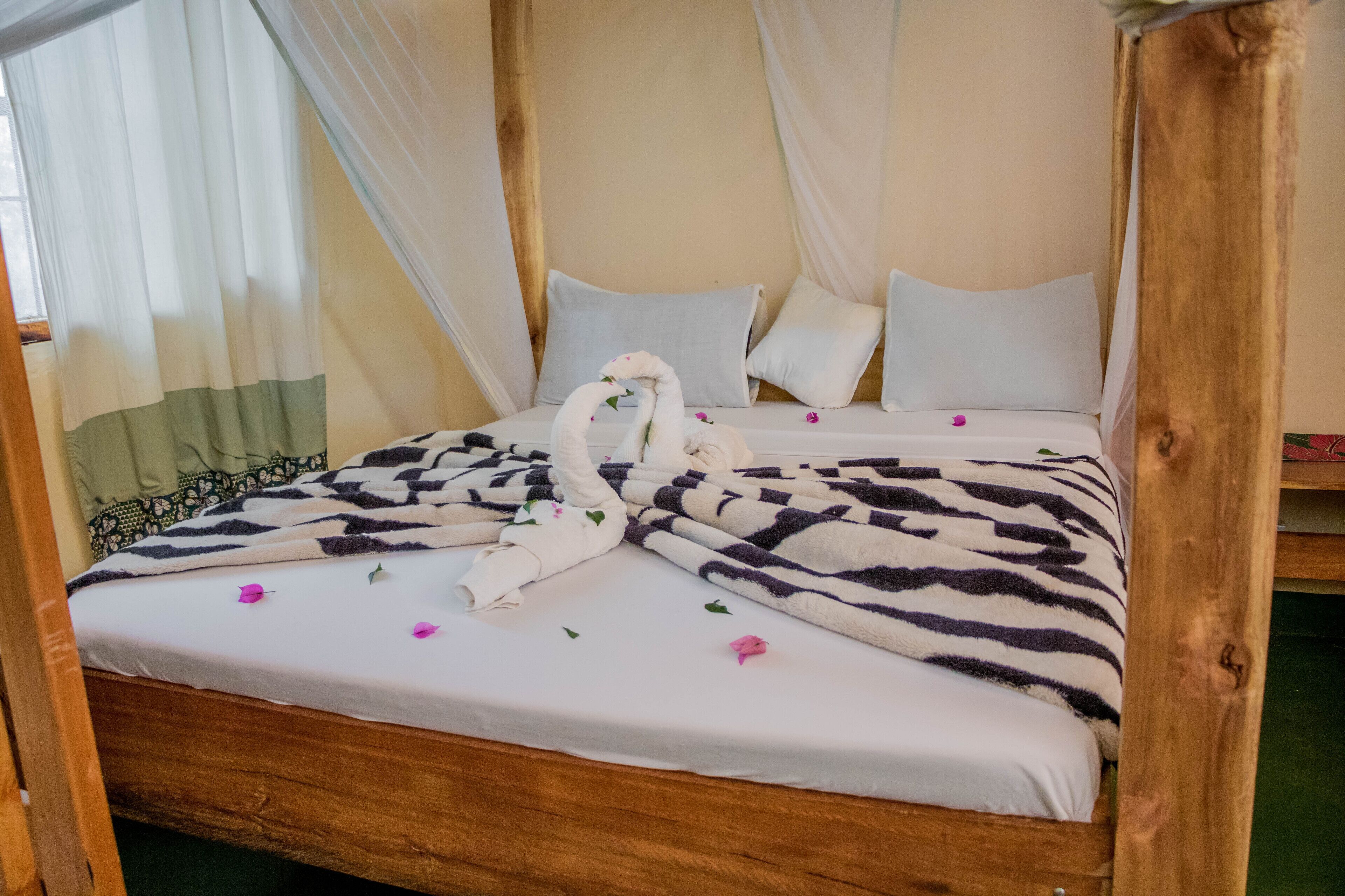 Una cama con sábana blanca, una manta de estampado de cebra y dos toallas con forma de cisne.