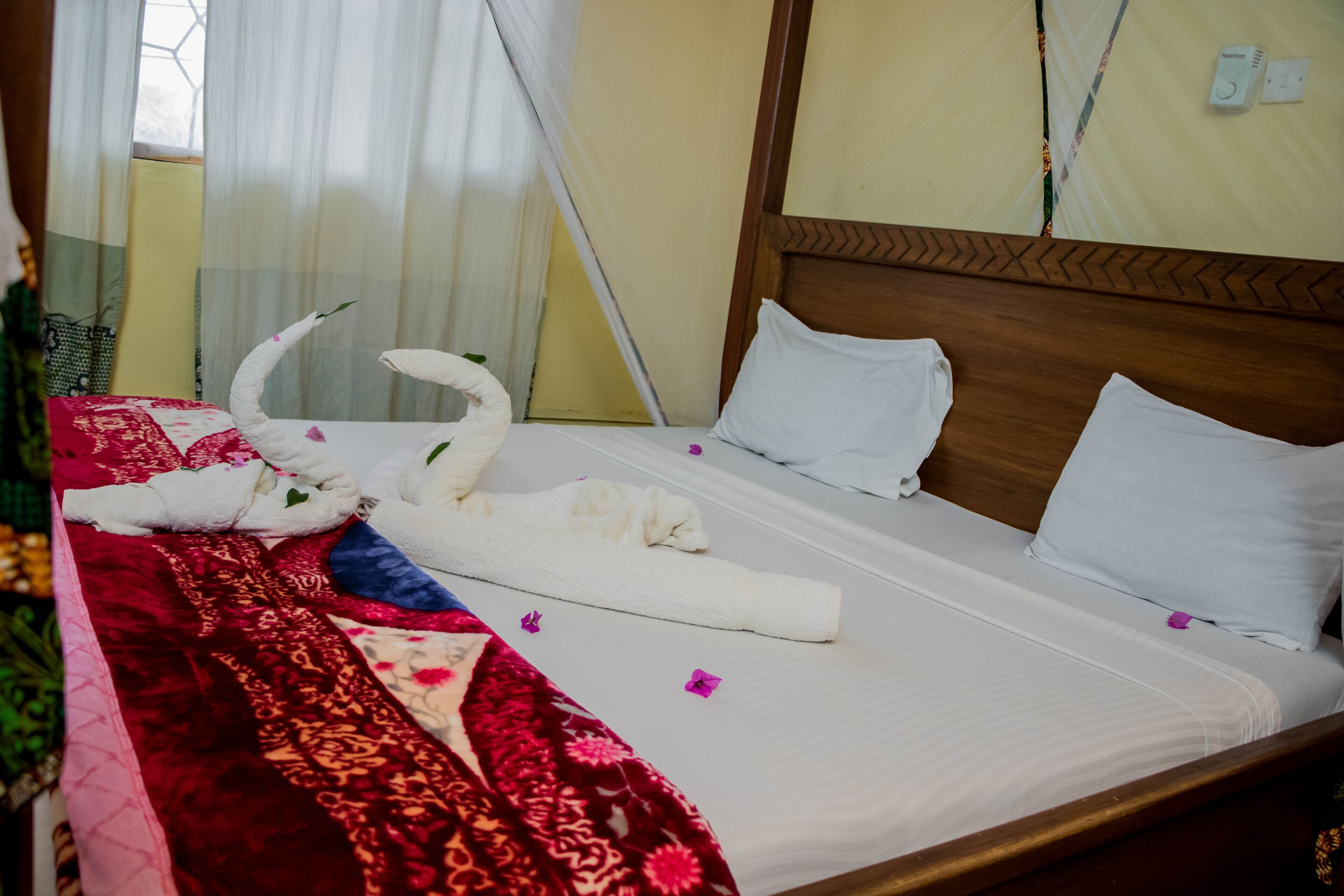 A neatly made bed with white linens, a red patterned bedspread, and a white towel with a swan design.