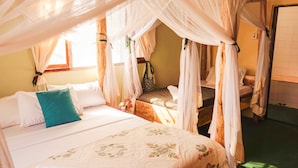 A room with a bed under a canopy, a small table with a chair, and a window with curtains. - The  Secret  Garden  Hotel  Moshi (Moshi)
