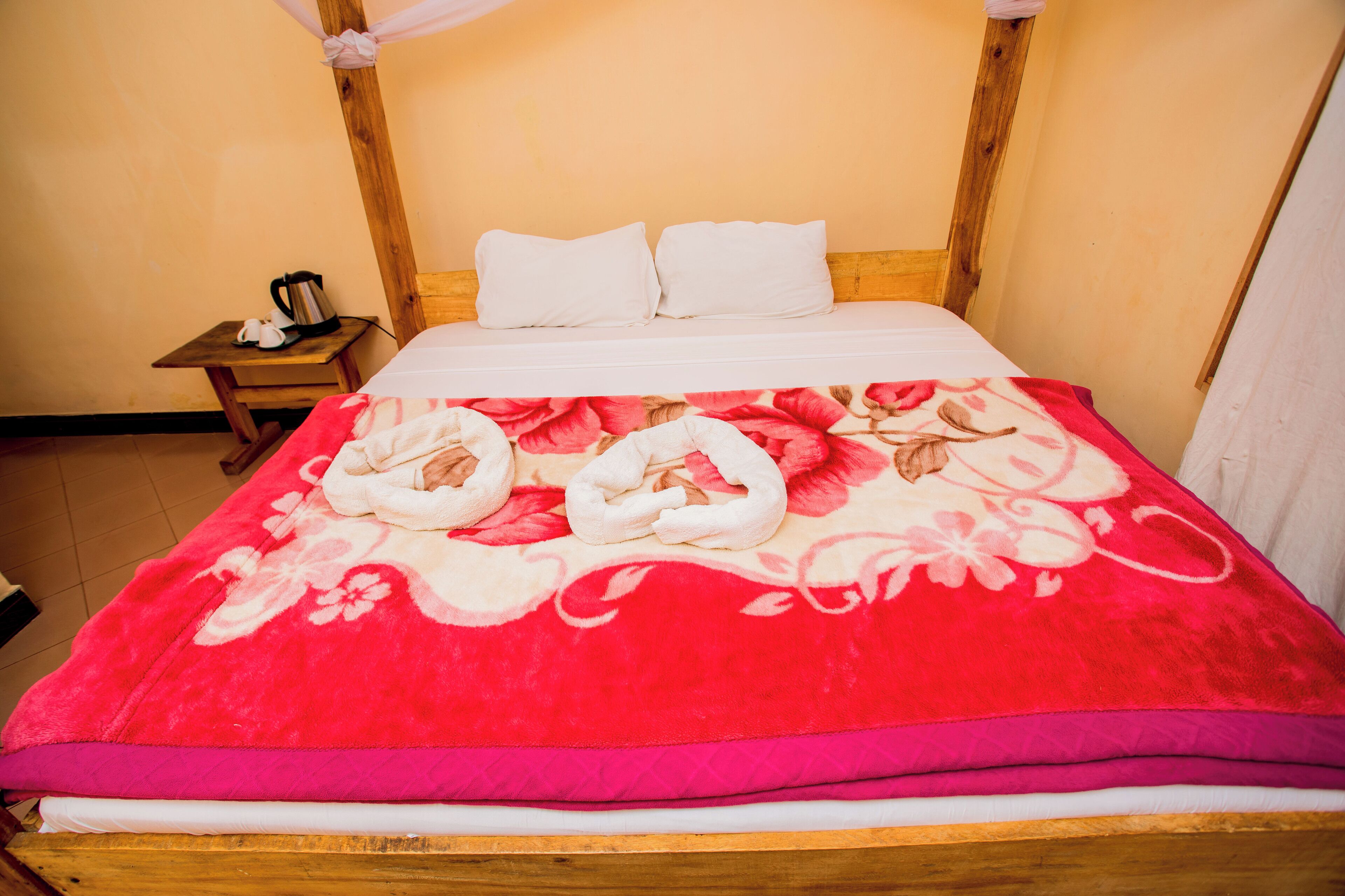 Een bed met een rode bedspreider met bloemenprint, een houten hoofdbord en witte kussens.