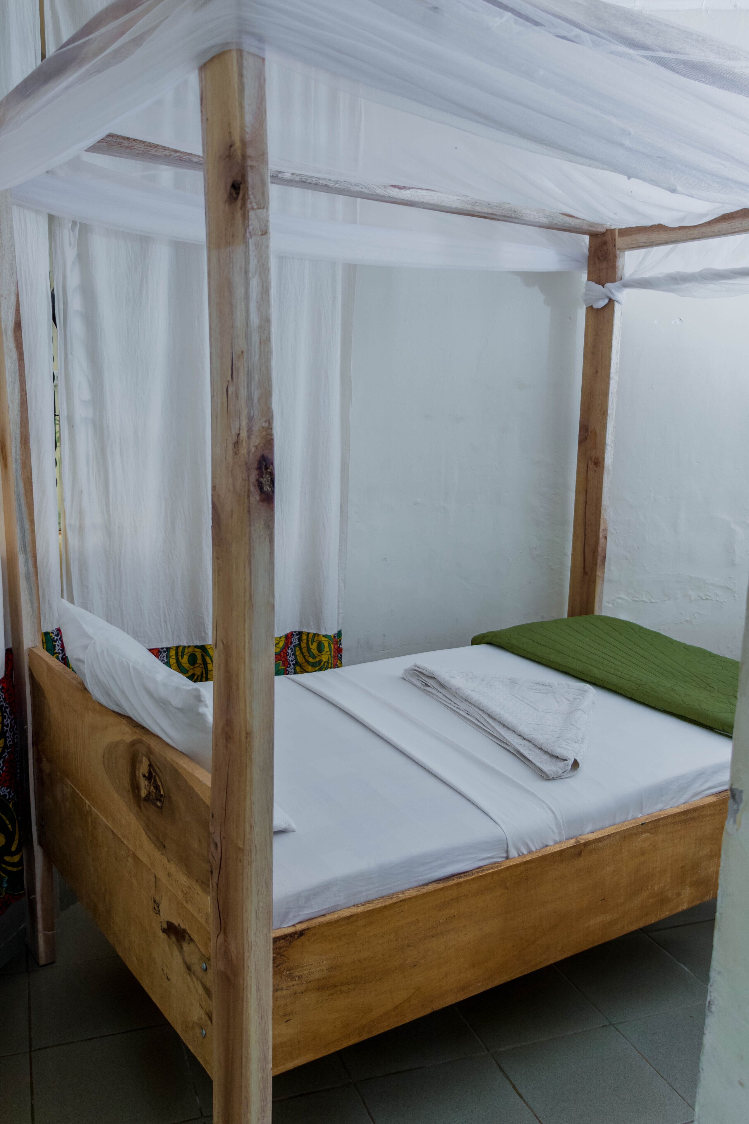 Ein hölzernes Himmelbett mit weißen Laken und einer grünen Decke.