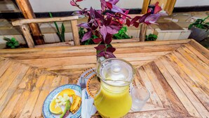 A wooden table with a glass pitcher of yellow drink, a plate with food, and a vase with purple flowers. - The  Secret  Garden  Hotel  Moshi (Moshi)