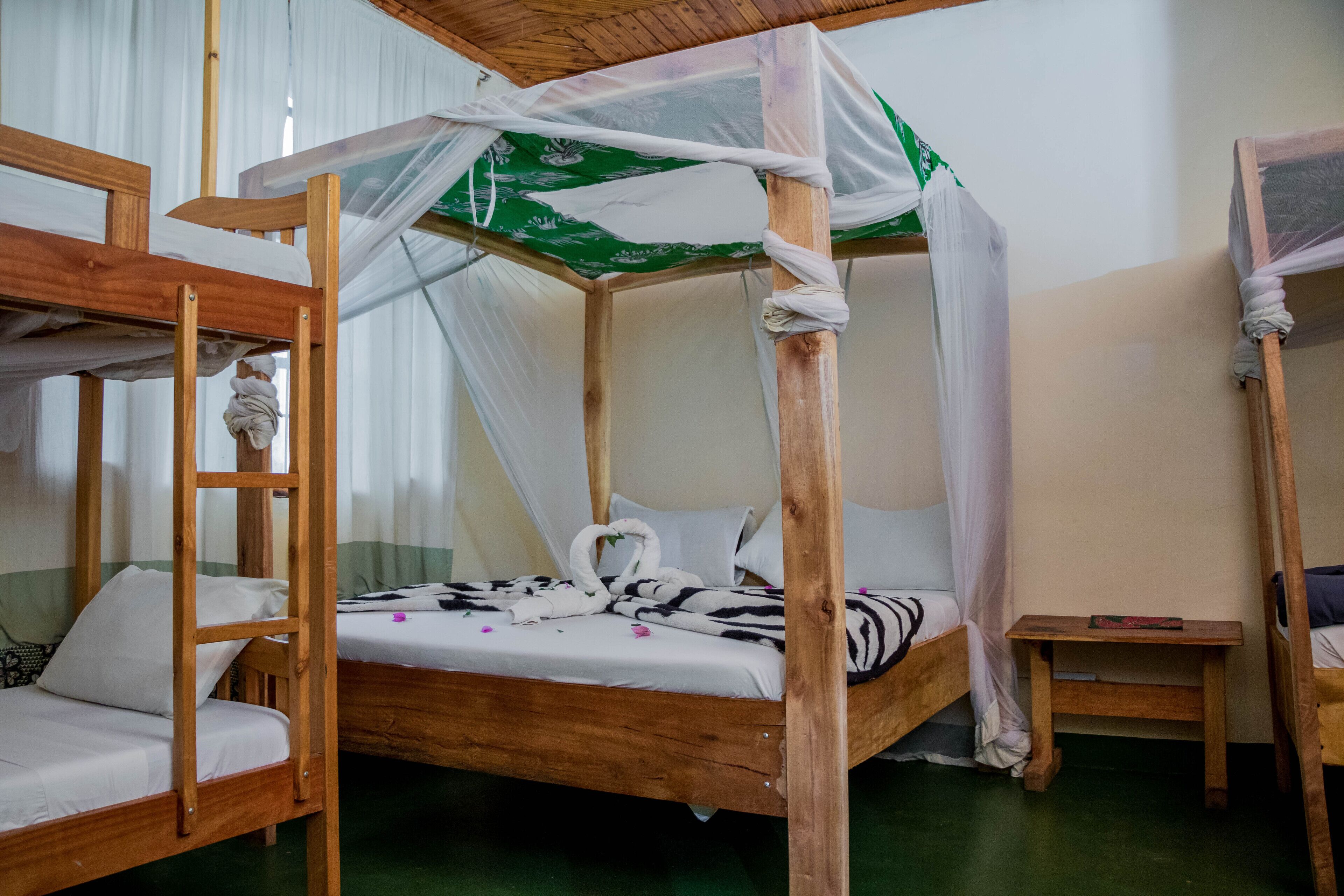 A room with a wooden four-poster bed, a smaller single bed, and a nightstand with a book.