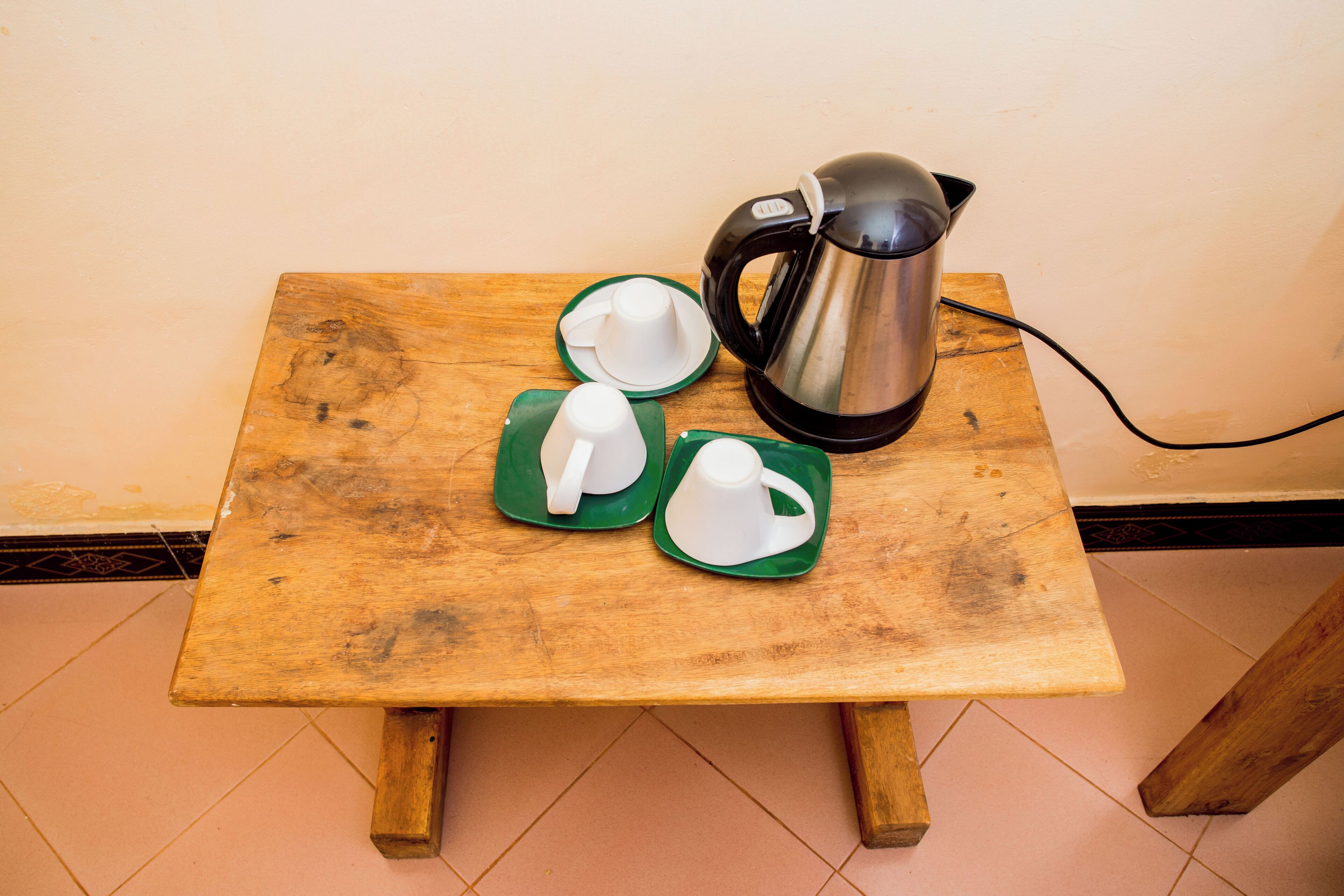 A small wooden table with a kettle, two white cups, and saucers on green plates.