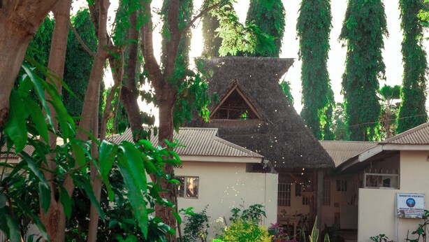 A building with a thatched roof, surrounded by lush greenery and tall trees. - The  Secret  Garden  Hotel  Moshi (Moshi)