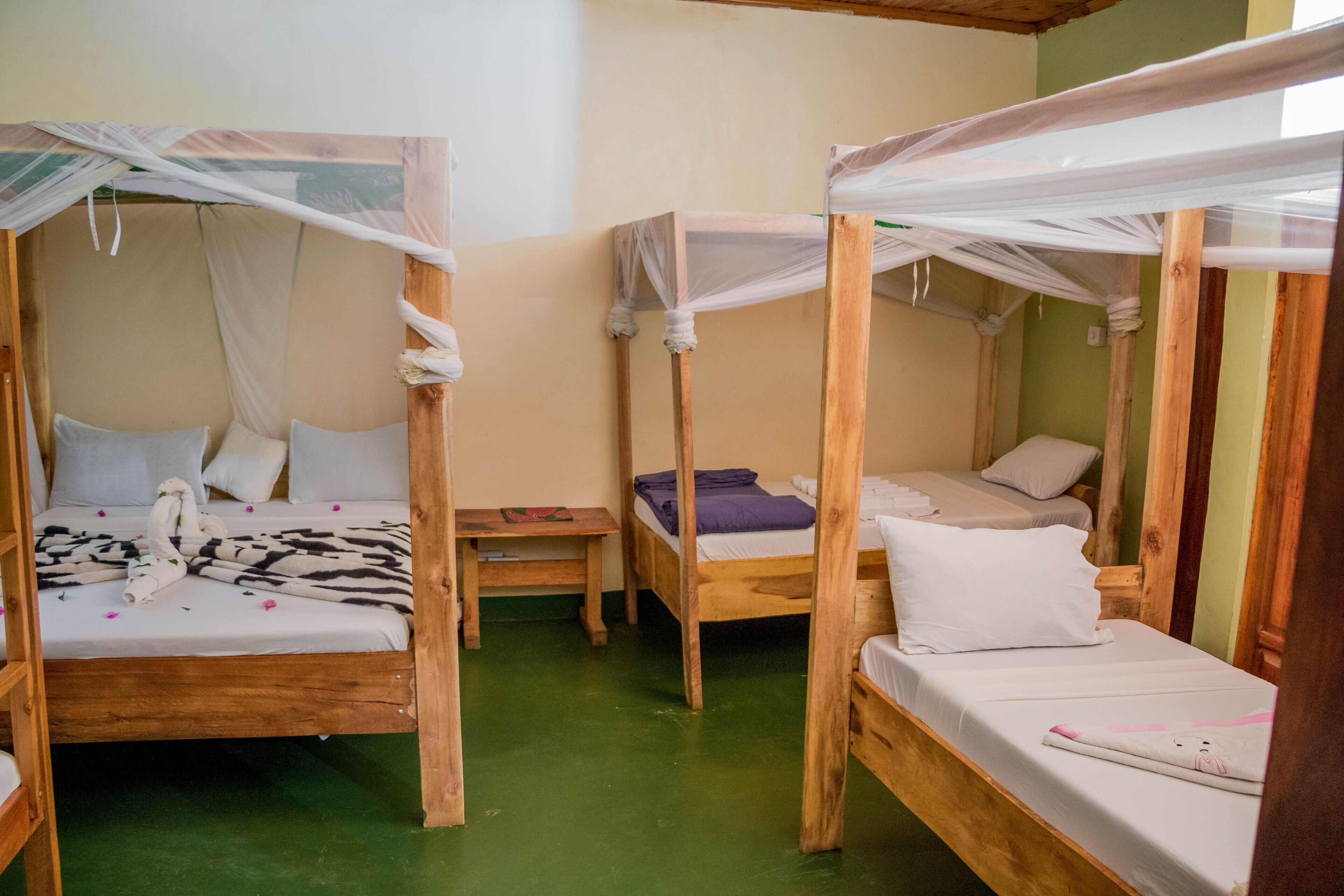 Una habitación con tres camas de madera, cada una con dosel. Hay una pequeña mesa de madera entre las camas.