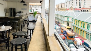 Un balcón con vistas a una calle concurrida y edificios. Hay mesas y taburetes en el balcón.