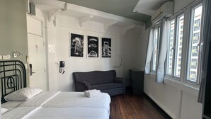Una habitación de hotel con una cama, un sofá gris, una mesita y un teléfono instalado en la pared.