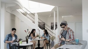 Un interior moderno con una escalera, una zona de comedor con una mesa redonda y una persona sosteniendo una cámara.