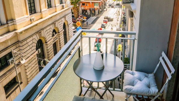 Een balkon met een tafel en twee comfortabele stoelen, met uitzicht op een straat met gebouwen en een palmboom.