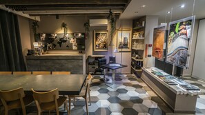 A modern restaurant with a black and white hexagonal tile floor, a central dining table with chairs, hanging plants, and a bar area with shelves and decorative items. - Vinto House Salerno (Salerno)