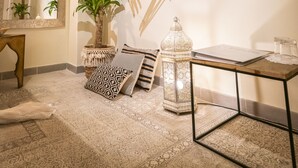Een kamer met een kamerbreed tapijt, een hangplant, een spiegel, een houten tafel en een decoratief object aan de muur.