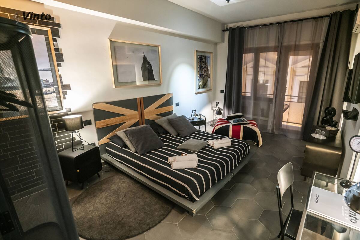 A modern hotel room with a large bed, a desk, a chair, and a view of the city.