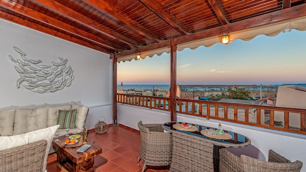A balcony with wicker furniture, a cushioned sofa, and a table set with plates and glasses. - Casa Sabbionara (Chania)